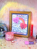 A beautiful framed art print sits beside a hand lettered mug, disco ball, and magic candle. The print features who hands, each holding a candy heart with hand lettering phrases "You're Cute" and "Be Mile" a rainbow connects the hearts and in the background are whimsical clouds, stars, and magical twinkles. A perfect gift for Valentine's Day, or just because for your lover, or any tarot enthusiast.