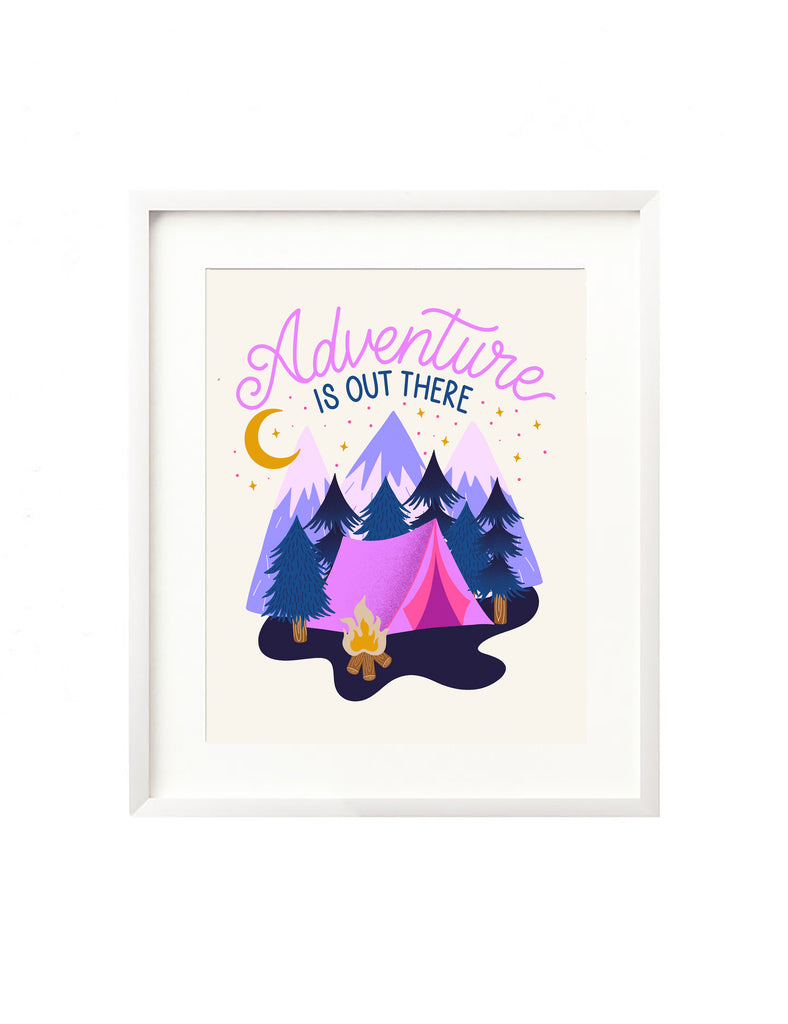 A framed art print - the illustration is of a vibrant pink tent and roaring campfire nestled in a whimsical forest scene. There are mountains in the background and the night sky is illuminated with a crescent moon and twinkling stars. Hand lettering spells out "Adventure is out there"