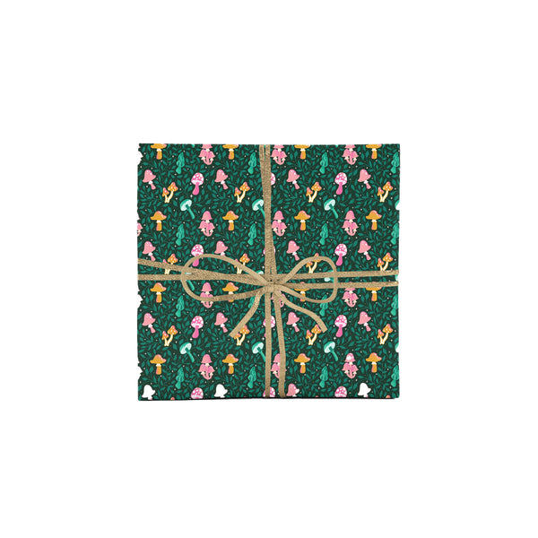 Photo shows a gift wrapped in whimsical hand illustrated wrapping paper - it has a festive mushroom pattern with various colorful mushrooms surrounded by greenery. The gift is wrapped with sparkly gold ribbon.