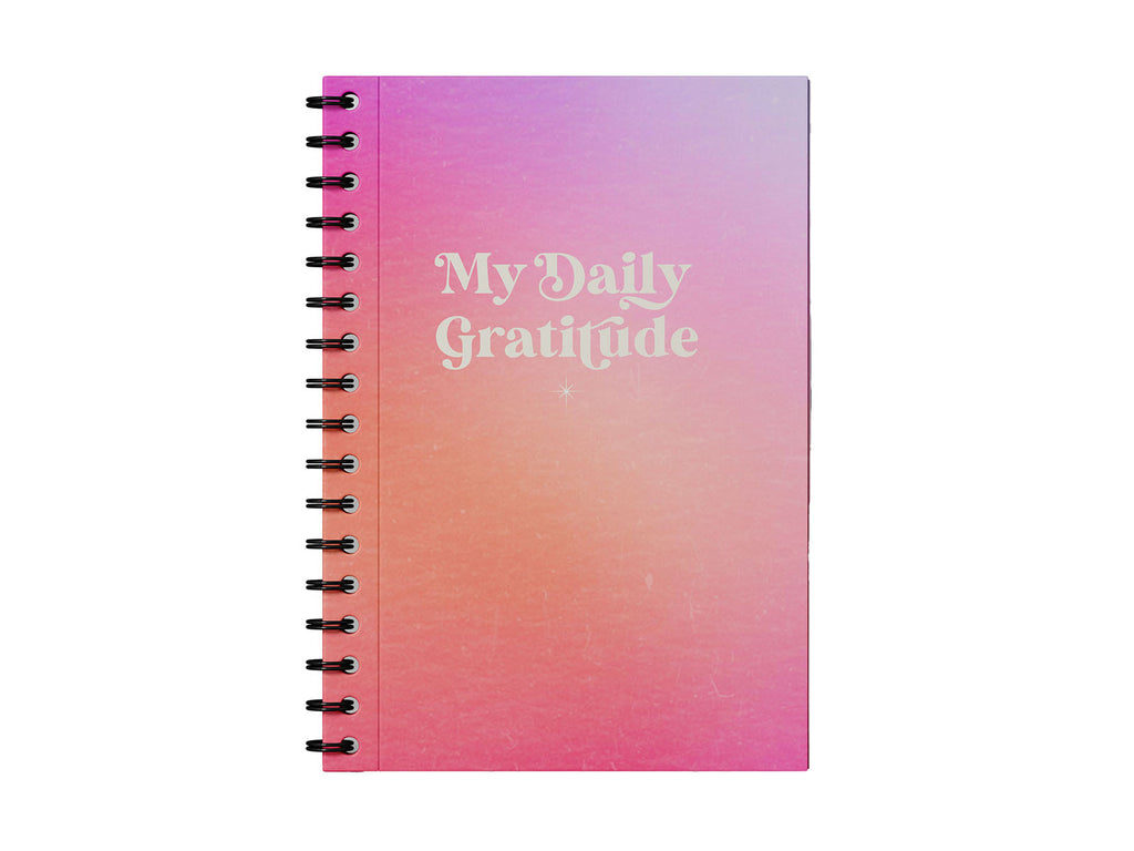 Photo shows a gratitude journal on a white background. The journal has a pink and purple aura ombre background and says "My Daily Gratitude" in a retro inspired lettering style. There is a twinkling white star on the cover. Inside are guided pages to reflect on what makes you grateful each day to cultivate and grow your mindfulness practice. Lovely bohemian, magical, yoga stationery.
