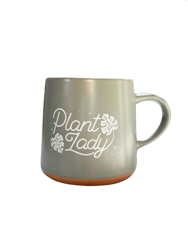 A beautiful natural sage green ceramic mug with natural clay bottom that says "Plant Lady" in a beautiful, handlettering script. There are monstera leaves incorporated into the lettering and framing it in, along with several twinkling stars around the image. A perfect gift for the plant lovers in your lives, with lots of house plants and house plant care at the forefront of their mind.