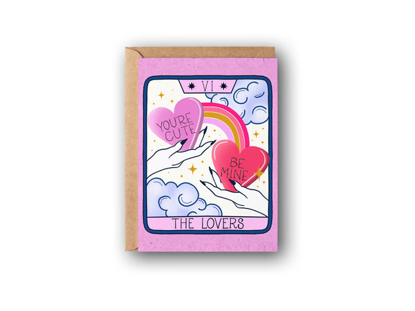A Valentine's Day Card is shown on a white background. The card features artwork inspired by The Lovers tarot card. There are two hands each holding a candy heart with hand lettering that says "You're Cute" and "Be Mine" A rainbow connects the hearts and in the background there are whimsical clouds and twinkling stars. A truly magical card to celebrate your love. Perfect for the magical witchy women, boho ladies, bohemain girlies in your life.