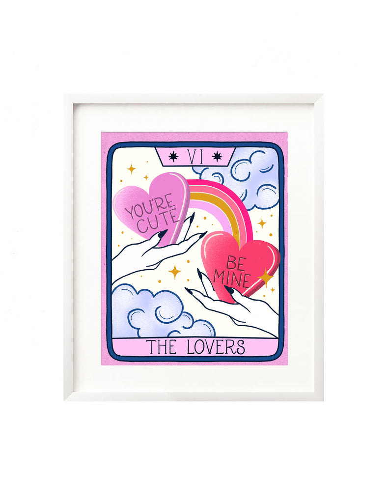 A love Valentine's Day art print sits in a white frame. The wall decor is an illustration of The Lovers tarot card. It features who hands, each holding a candy heart with hand lettering phrases "You're Cute" and "Be Mile" a rainbow connects the hearts and in the background are whimsical clouds, stars, and magical twinkles. A perfect gift for Valentine's Day, or just because for your lover, or any tarot enthusiast.