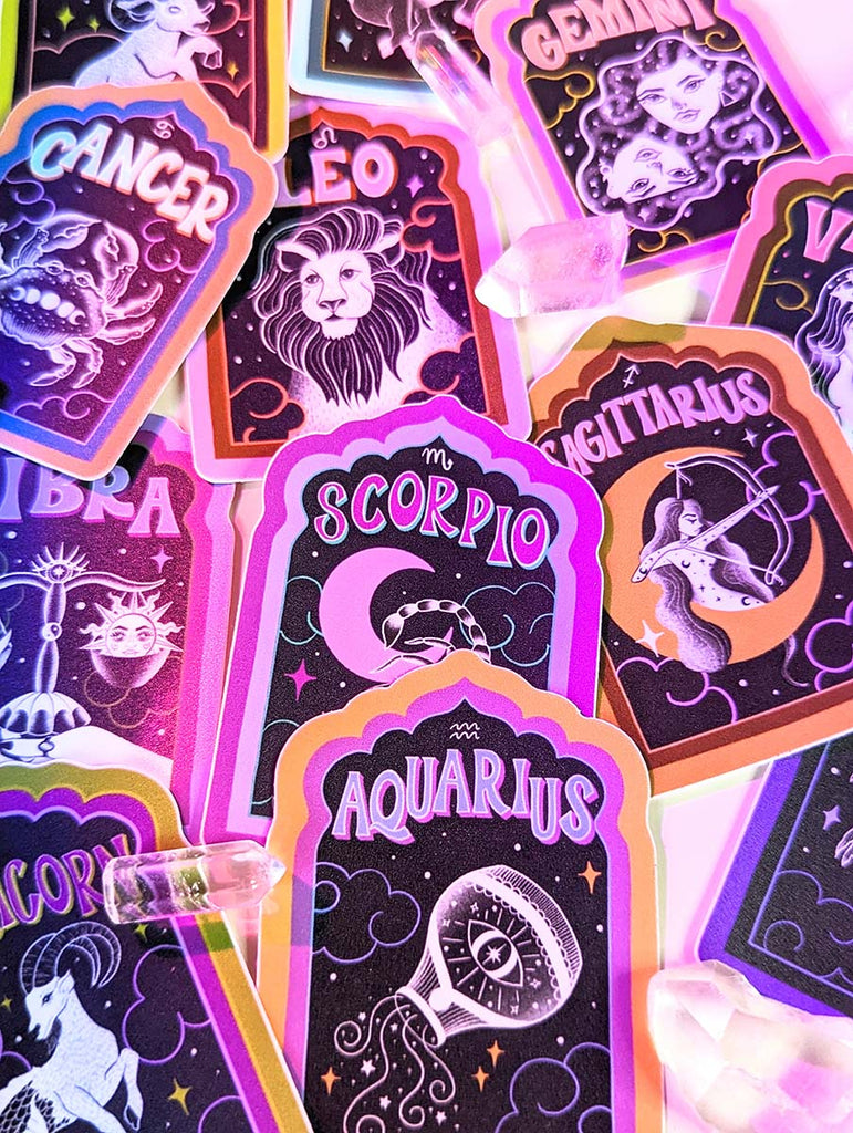 A collection of hand illustrated stickers sits atop notebook pages surrounded by clear quartz crystals. There are astrological stickers for each zodiac sign. Aries, Taurus, Cancer, Gemini, Leo, Virgo, Libra, Scorpio, Sagittarius, Capricorn, Aquarius, Pisces. There are Mushroom stickers, snake stickers, flower stickers, rainbow stickers. All with uplifting hand lettering messages. Witchy. Witch. Boho. Cowgirl. Western. Disco Cowgirl. Cosmic Cowgirl. Magical. Bohemian. Yoga. Yogi.