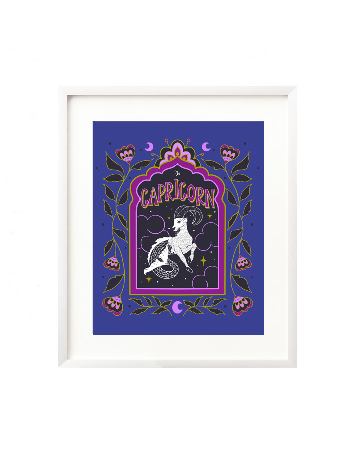 A framed art print - the illustration is a depiction of the Capricorn zodiac sign. The celestial sea goat is illustrated floating in a starry night sky, surrounded by whimsical clouds and framed in by folk art flowers. Capricorn is hand lettered at the top in a bold, groovy, retro inspired style.