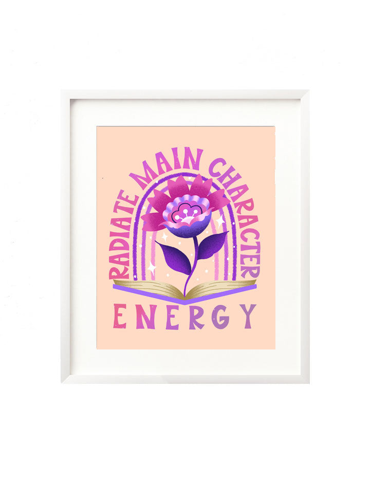A framed art print - the illustration features a bright, vibrant pink and purple flower emerging from the pages of an open book. There is a radiant purple and pink rainbow in the background with twinkling stars all around. Hand lettered is the message "Radiate main character energy" in a bold, retro inspired style.