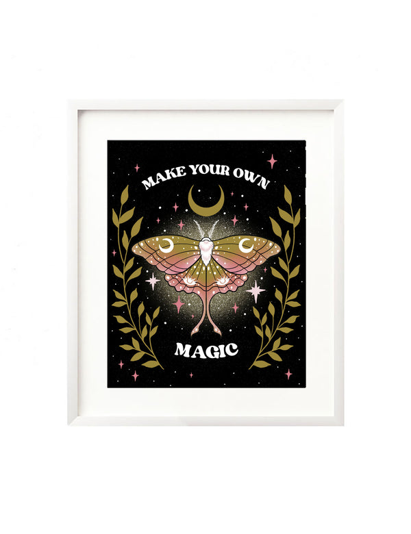 A framed art print - the illustration features a cosmic moth with moons, twinkes, and intuitive eyes encased in it's pink and yellow wings. It is surrounded by whimsical greenery, twinkling stars, and a crescent moon. Above and below the illustration hand lettering spells out "Make your own magic"