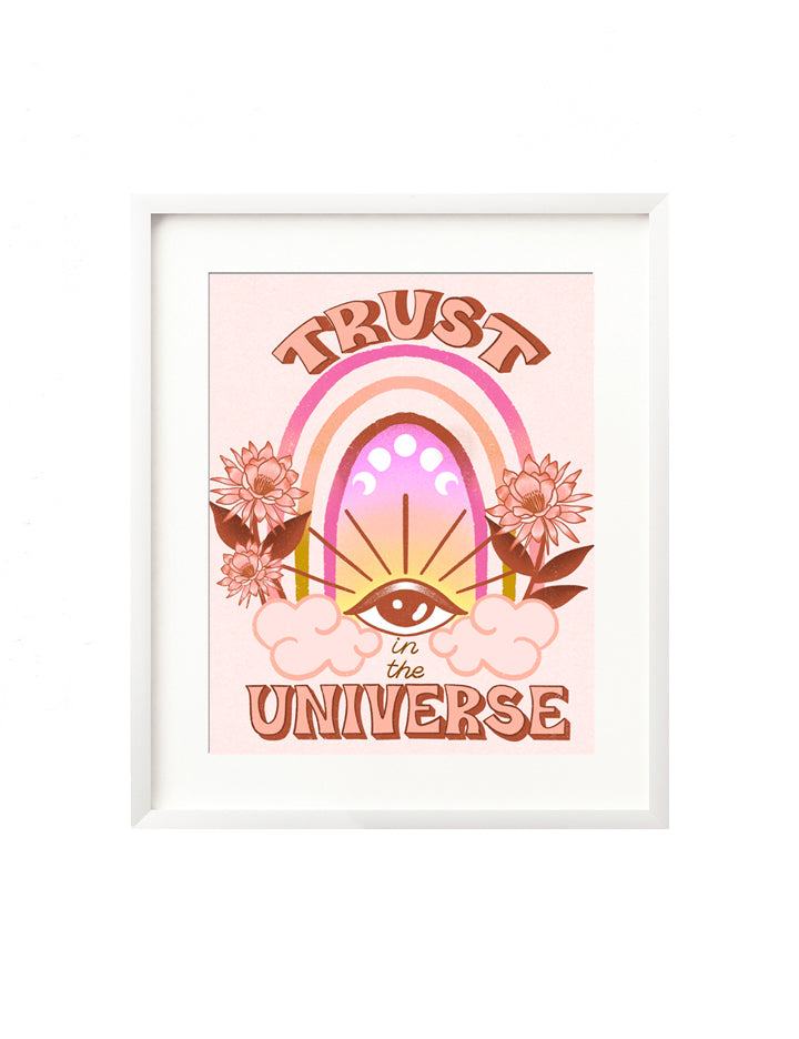 A framed art print - the illustration features an intuitive eye in the clouds with a vibrant rainbow of pinks, yellow, and orange behind. There are vibrant florals framing it in, and moon phases above the eye. In hand lettering "Trust in the Universe" frames the scene in a bold retro inspired style.