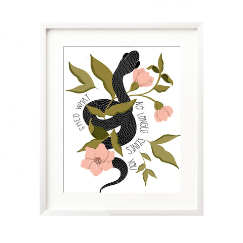 A framed art print - the illustration is of a black snake coiled and slithering through vibrant pink florals and greenery. Hand lettering spells out "Shed what no longer serves you" on either side.